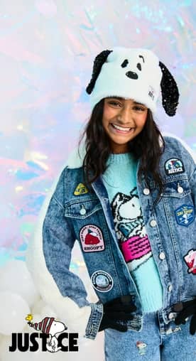 Girl wearing Snoopy ear hat, denim jacket with playful patches, and blue sweater with Snoopy graphic.
