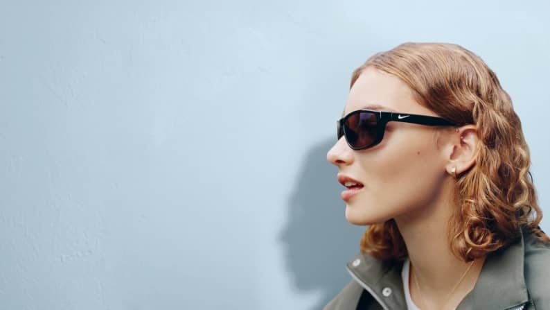 Adult wearing dark rectangular sunglasses and a casual jacket in profile.