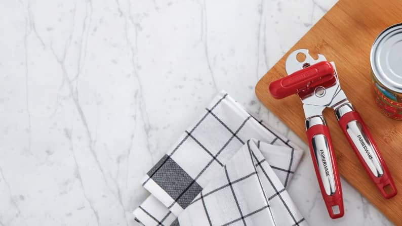 A red can opener and a black and white grid patterned towel on a marble counter and wood board. Reads: Kitchen gadget upgrades.