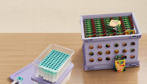 Glue and crayons in clear and purple boxes on a wood desk.