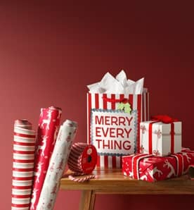 Image of a wooden bench with holiday-themed gift bags, wrapping paper and ribbons.
