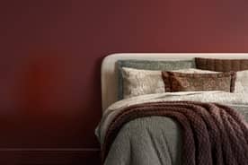 A bed set with patterned pillows and a throw blanket, next to a nightstand with a lamp.