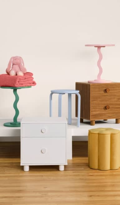 A white bed frame, colorful wavy side tables and a wooden nightstand on a wood floor. Reads: From twenty-nine ninety-seven. Kid-approved furniture