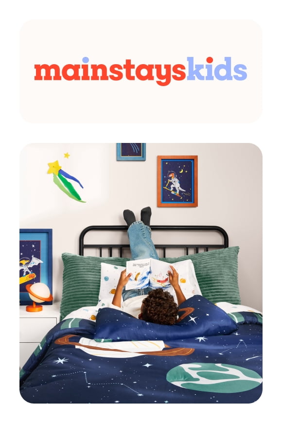 boy sitting on his twin bed on top of a galexy bedspread from the explore & roar collection. space dinosaur wall art and a grey ribbed body pillow.