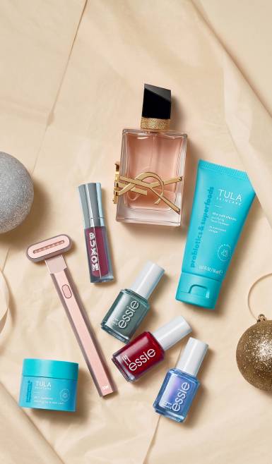 Tula skincare, Essie nail polishes, Buxom lip gloss, a facial razor and a perfume bottle arranged as holiday beauty gifts.
