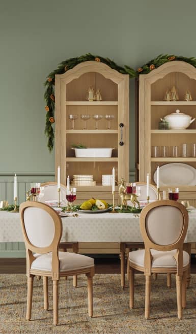 A sage green dining room features two hutches and a dining table set adorned with tableware and decor.