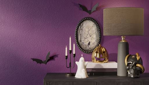 Image of dark console table decorated with a ghost, skull, and gold jack-o-lantern. The wall is a deep purple.