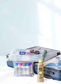 Toothpaste, sunscreen, sunglasses, a swimsuit, travel bottles and a towel inside a suitcase, sitting on a bed.