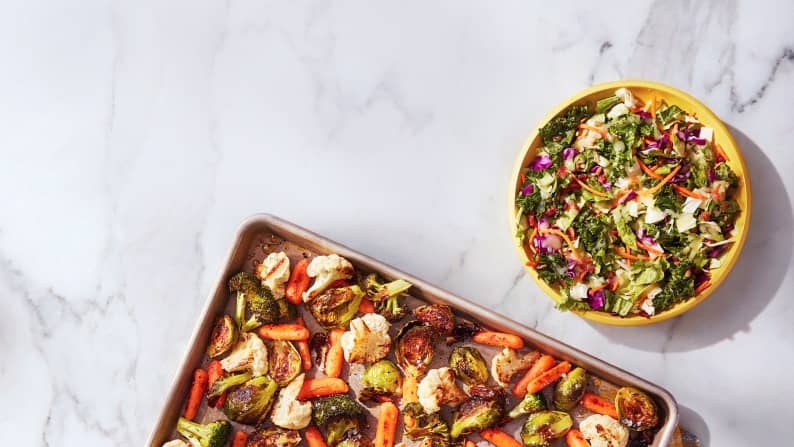 Prepared meal tray with vegetables and a salad bowl on a white surface.