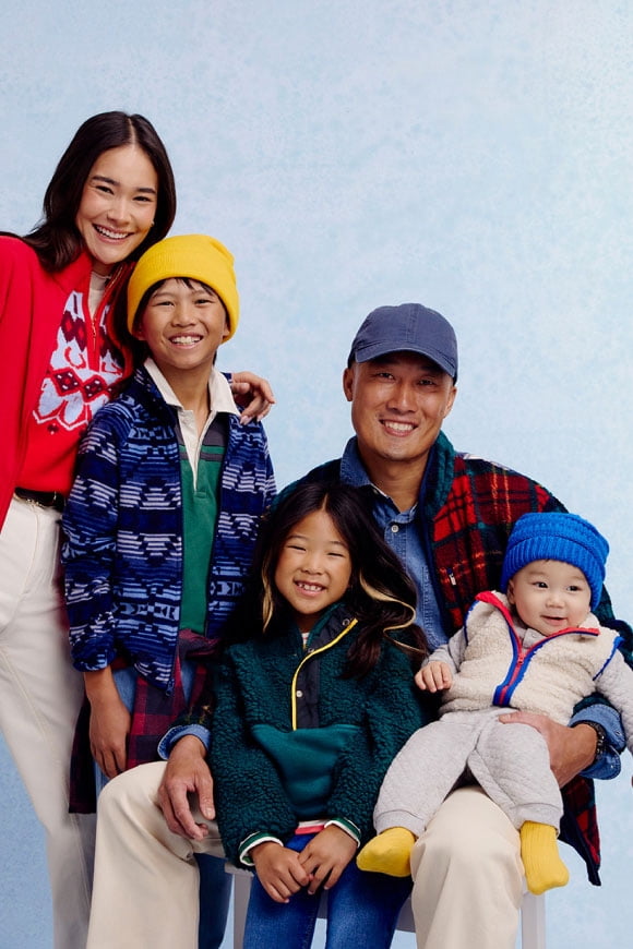 A family of two adults and three children in colorful fleece and winter layers smiles together.