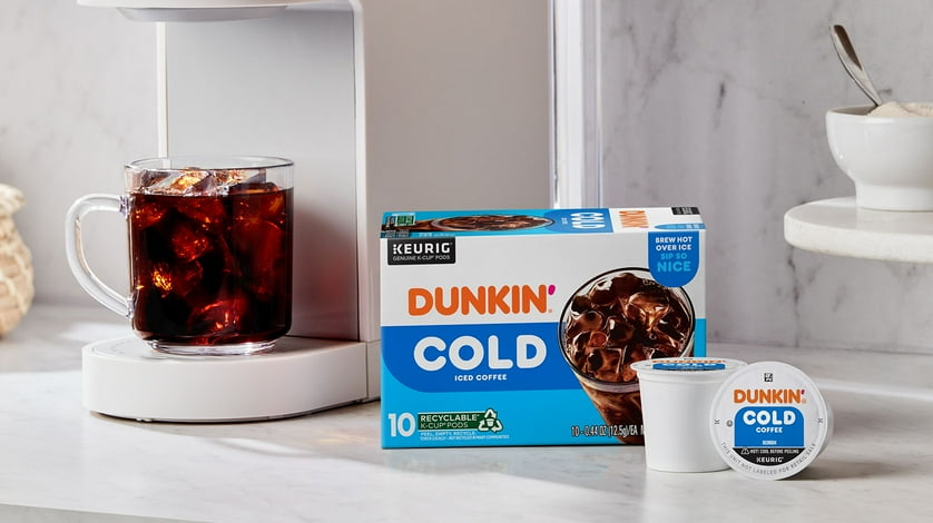 A box of Dunkin' Cold coffee k-cups, behind to k-cups and in front of the beverage made.