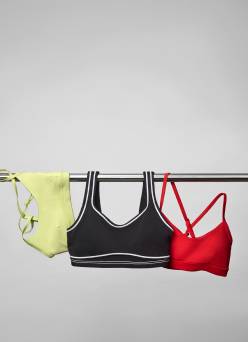 A green sports bra, a black sports bra and a red sports bra are draped over a metal bar.