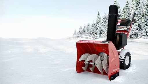 Snowblower in snow with trees in the background.