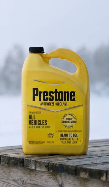 Prestone antifreeze and coolant jug for all vehicles on a wooden surface in a snowy outdoor setting.
