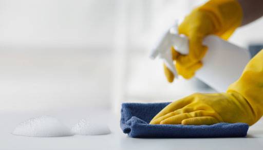 An image of hands wearing yellow cleaning gloves spraying cleaner and wiping a counter with a towel.
