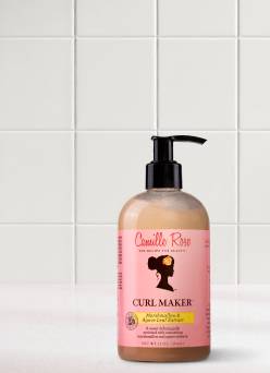 A bottle of Camille Rose Curl Maker hair product with marshmallow and agave leaf extract is on a marble tabletop with a tile background.