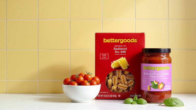 : A bowl of tomatoes, a box of bettergoods pasta, and a jar of bettergoods pasta sauce on a kitchen counter.