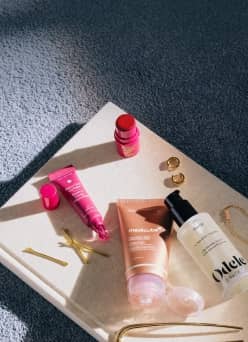 Odette skincare bottle and other beauty products on a stone tray with gold rings and hairpins.
