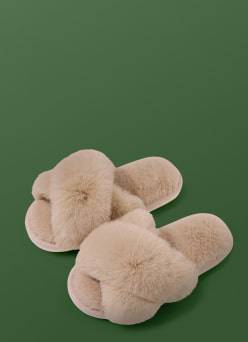 A pair of fluffy beige slippers with soft faux-fur texture, displayed against a dark green background.