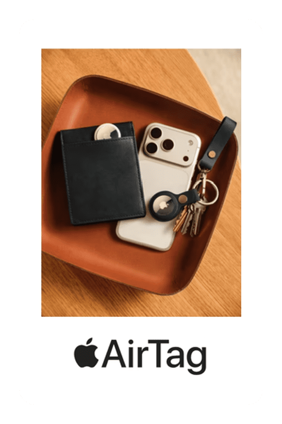 Image shows an AirTag with accompanying leather case and loop, displayed with a phone and keys, on a wooden background.