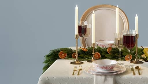 A linen-draped table is shown with a place setting, decor and a chair against a slate blue wall.