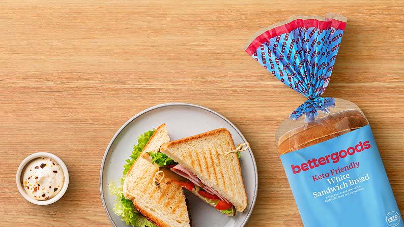 A grilled sandwich on a plate with a ramekin of white sauce next to a loaf of bettergoods keto-friendly white sandwich bread.