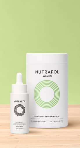 A white and black bottle of Nutrafol women's hair serum and a white and green jar of Nutrafol women's hair growth nutraceutical on a wood counter.