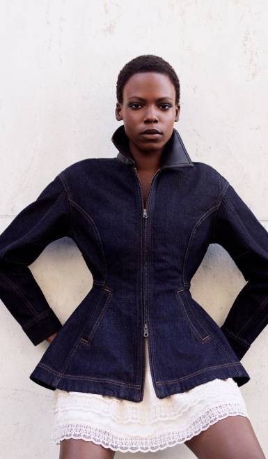 Woman in a dark denim peplum jacket over a white lace-trim mini skirt.