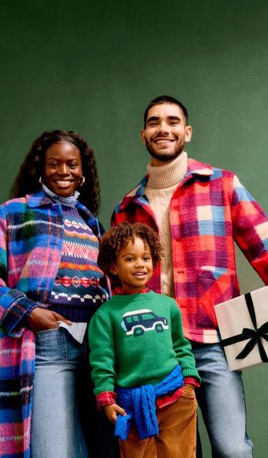 Three people in colorful winter outfits stand together, with one holding a wrapped gift box.