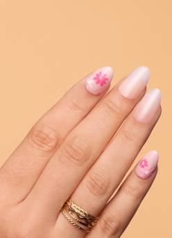 Model shot showing a hand with pastel pink and nude featuring small flower designs with text "Just-in nails, from $9. Shop now.”