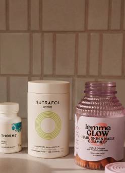 Assorted vitamin bottles from Nutrafol, Lemme and more arranged on a countertop in a softly lit kitchen setting.