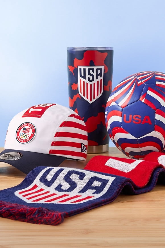 A variety of Team USA memorabilia is on a wooden counter—a baseball cap, a scarf, a metal water bottle and a soccer ball.