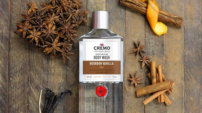 A bottle of Cremo body wash next to sticks of cinnamon and star anise on a wooden table