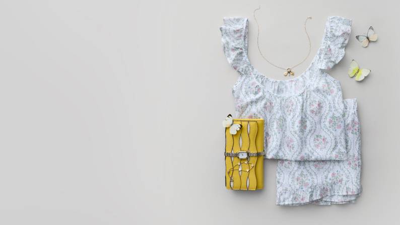 A printed pajama set, a yellow wallet, a gold watch, a gold necklace and gold bracelet are layered.