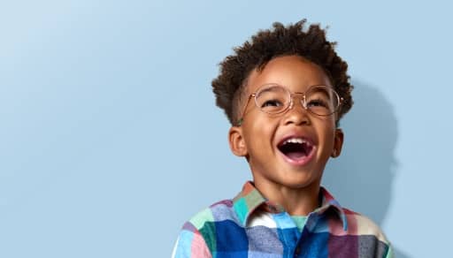 Child wearing round eyeglasses smiles in a colorful plaid shirt.