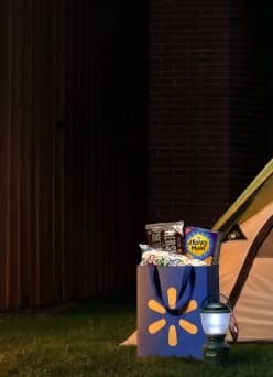 Express Delivery. A tent outdoors next to a lantern and a Walmart bag filled with chocolate bars, graham crackers and marshmallows.