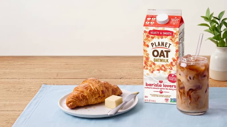 A carton of Plant Oat barista lovers milk next to an iced coffee and croissant.