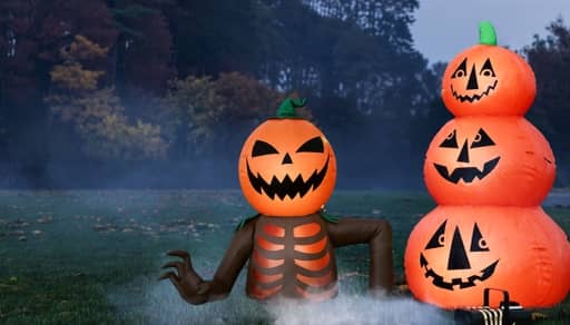 Inflatable jack o lantern with ribcage and arm beside stacked smiling pumpkin inflatables on a foggy lawn.