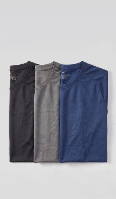 Three folded crew neck t shirts in black, gray and blue arranged side by side.