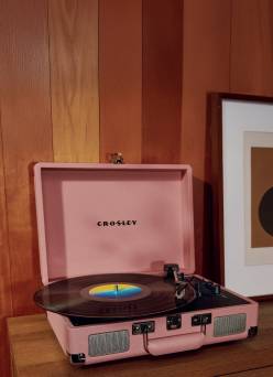 Pink suitcase-style Crosley record player with a vinyl record spinning on a wooden surface.