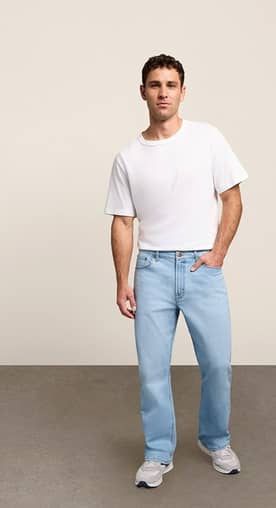 A mean wearing jeans and a white tee shirt is pictured on a beige backdrop.