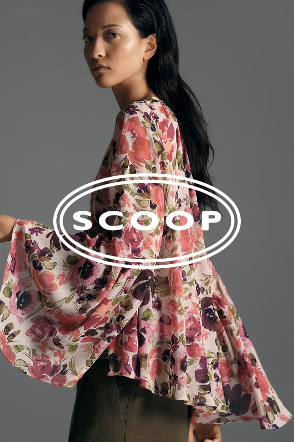 Woman with dark hair wearing a pink floral blouse with a fluid silhouette and flowing bell sleeves shown in profile against a gray background.