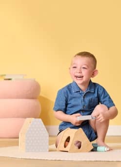 A smiling toddler sitting down next to wooden toys.