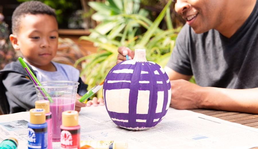 Father and son painting purple stripes on a white pumpkin