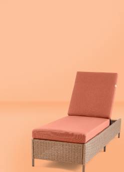A light brown woven patio set including a loveseat and two chairs with salmon cushions and a coffee table. Potted plants, a rug, and throw pillows.
