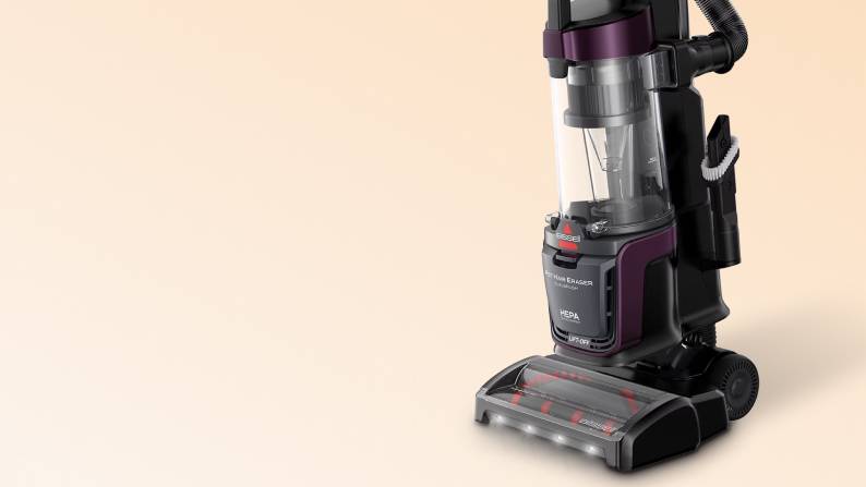 Bissell upright bagless vacuum cleaner with clear canister, purple accents, hose attachment and front LED lights.