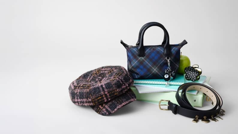 A checked hat, a checkered bag with charms and a black belt with charms are stacked on top of notebooks.