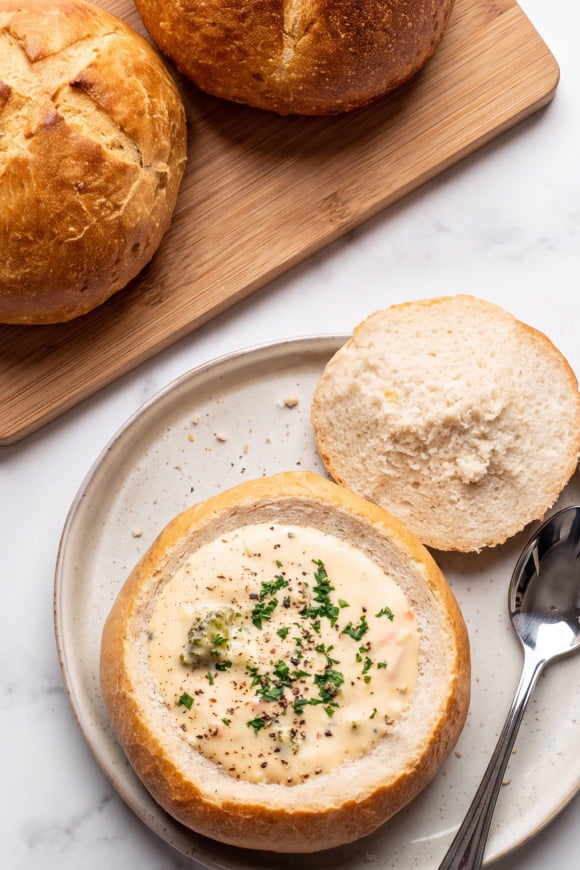 A bread bowl filled with soup is shown on a plate, next to 2 uncut bread bowls.