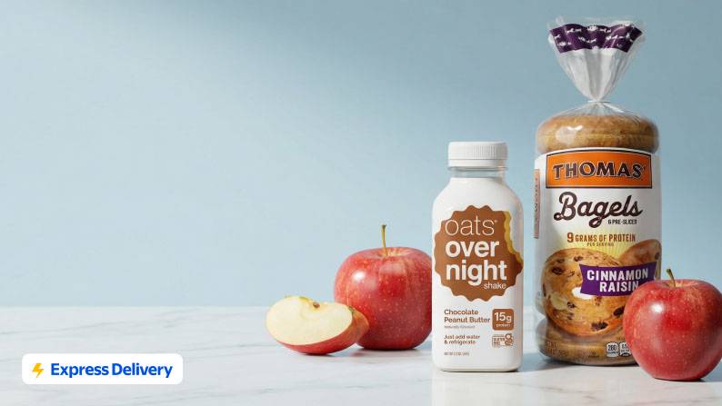 Apples, Oats Over Night chocolate peanut butter flavor, and Thomas’ cinnamon raisin bagels on a marble counter.