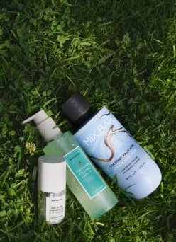 Three skincare bottles lying on fresh green grass.
